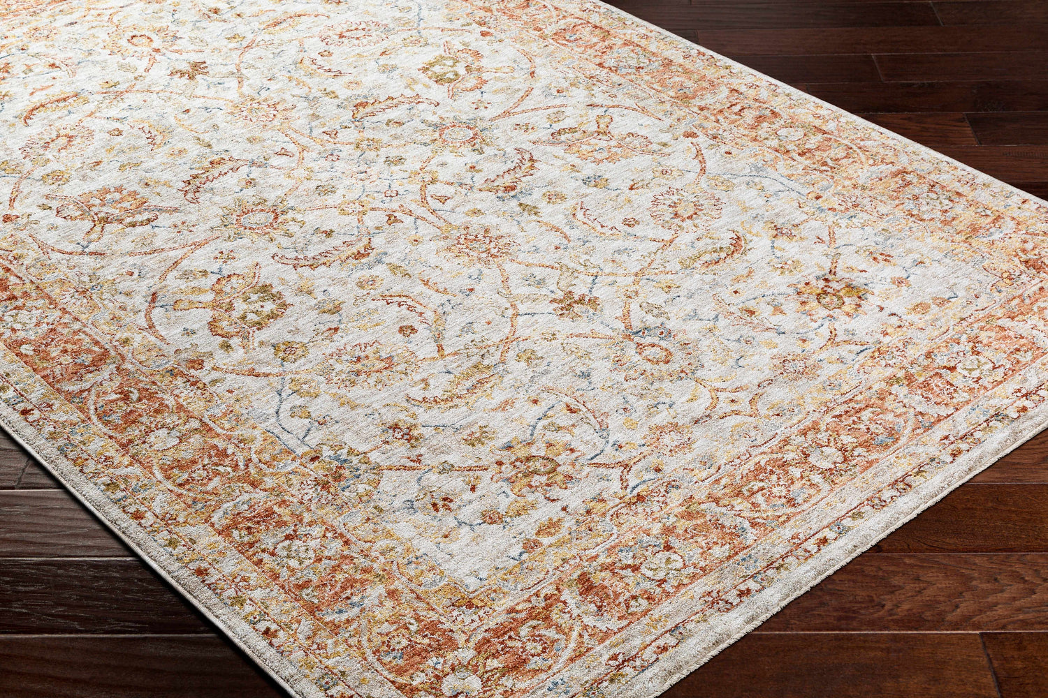 Close-up of the Dyan Cream Textured Rug with Fringes on dark wood floors. Features brick red, mustard, and blue floral pattern. Corner