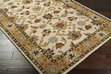 Close-up of the Smoot Area Rug. Beige rug with brown, olive, and blue floral and leaf pattern on dark wood floors. Corner