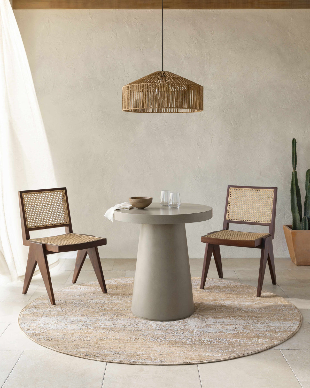 Dining room scene with a round tan Jehan Area Rug, concrete table, and wooden chairs. Roomscene-Round