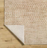 Close-up of the tan Kamin Area Rug showing its geometric pattern and soft texture on a light wood floor. Fold