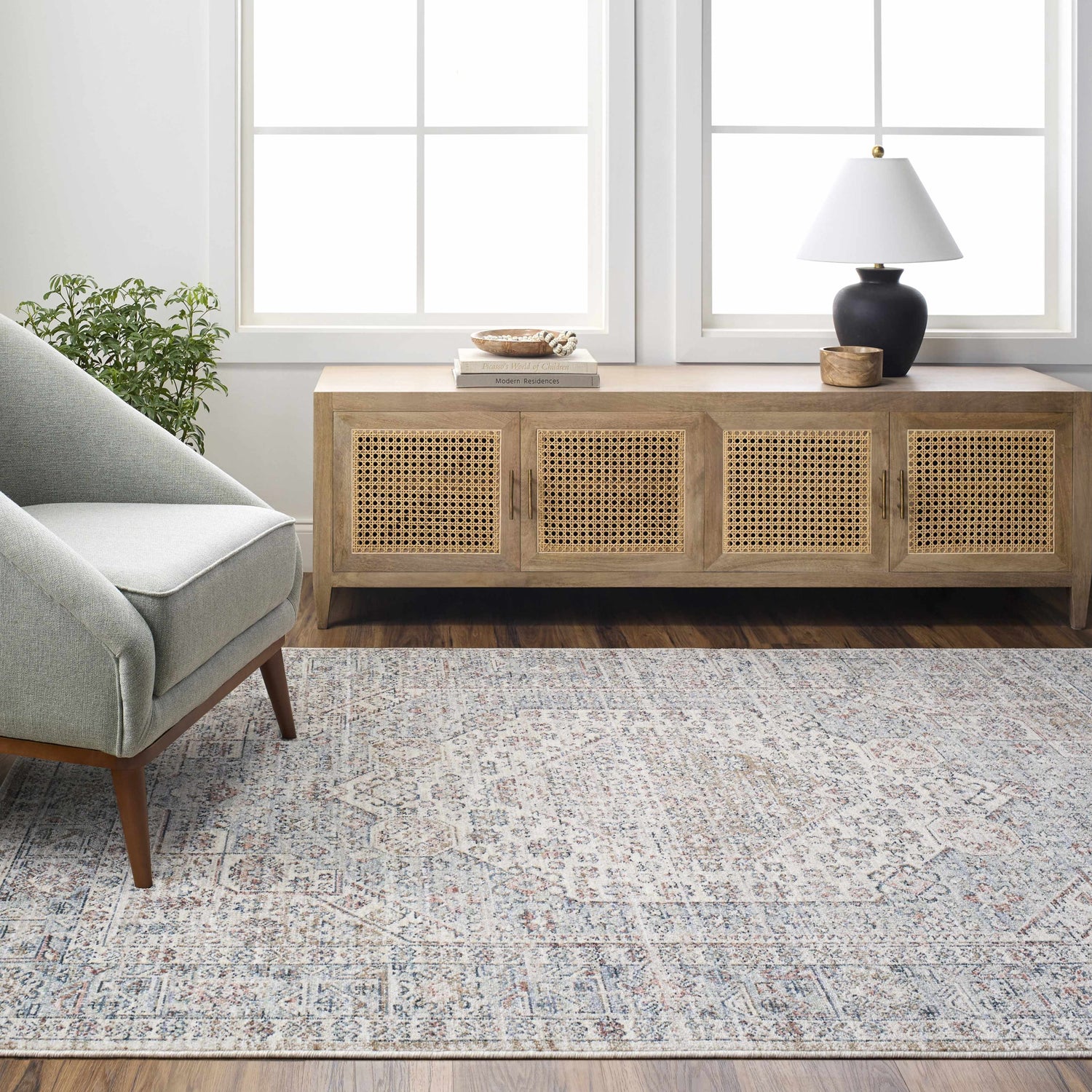 Living room scene with Kalei Beige & Blue Area Rug, light gray chair, wood cabinet, and natural light from large windows. Roomscene-Rectangle