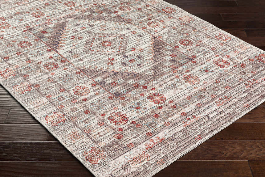 Close-up of the Liam Area Rug in Beachhouse. Traditional floral pattern in red, brown, and gray on dark wood floor. Corner