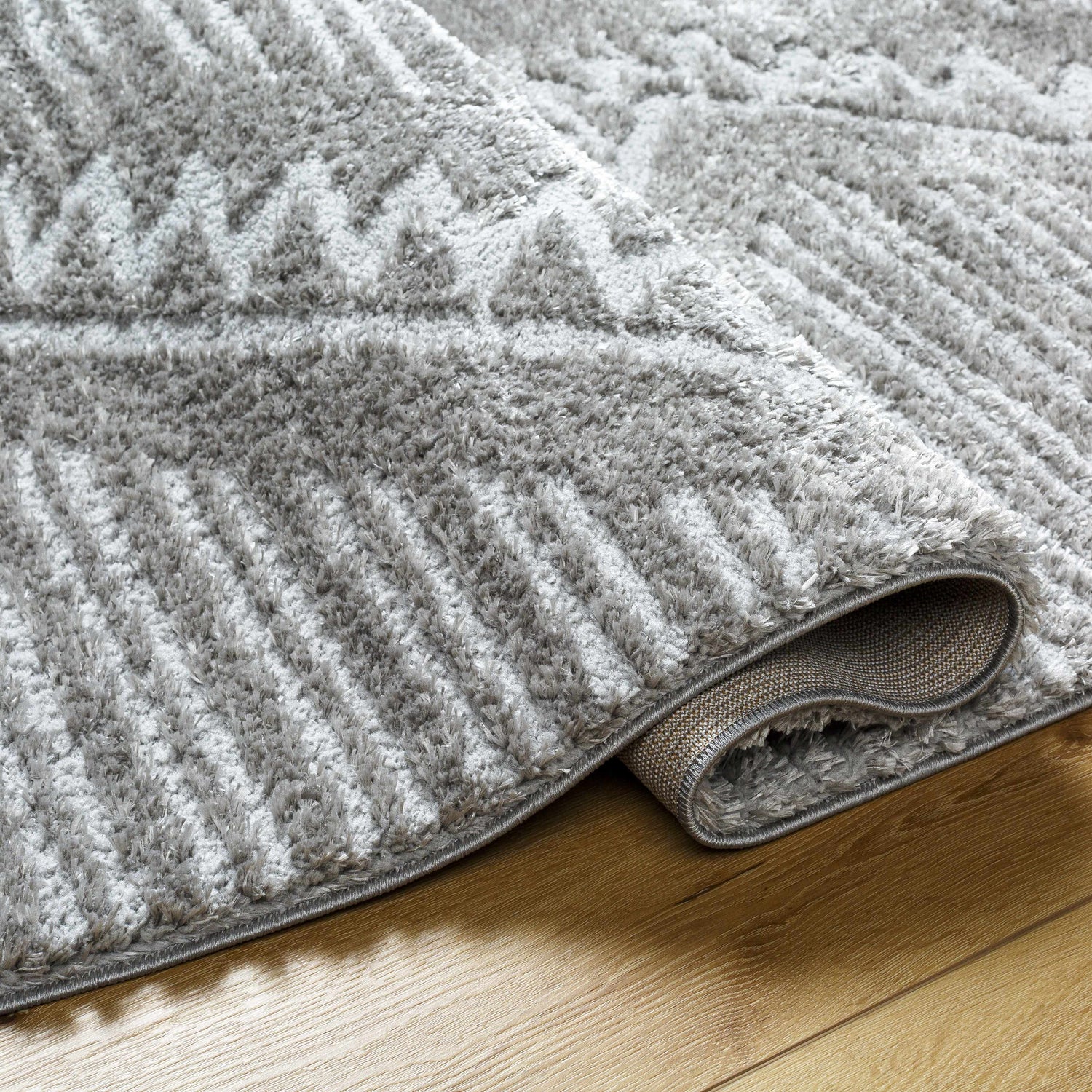 Close-up of the gray Edsel Area Rug showing its shag texture and geometric pattern on a wood floor. Fold