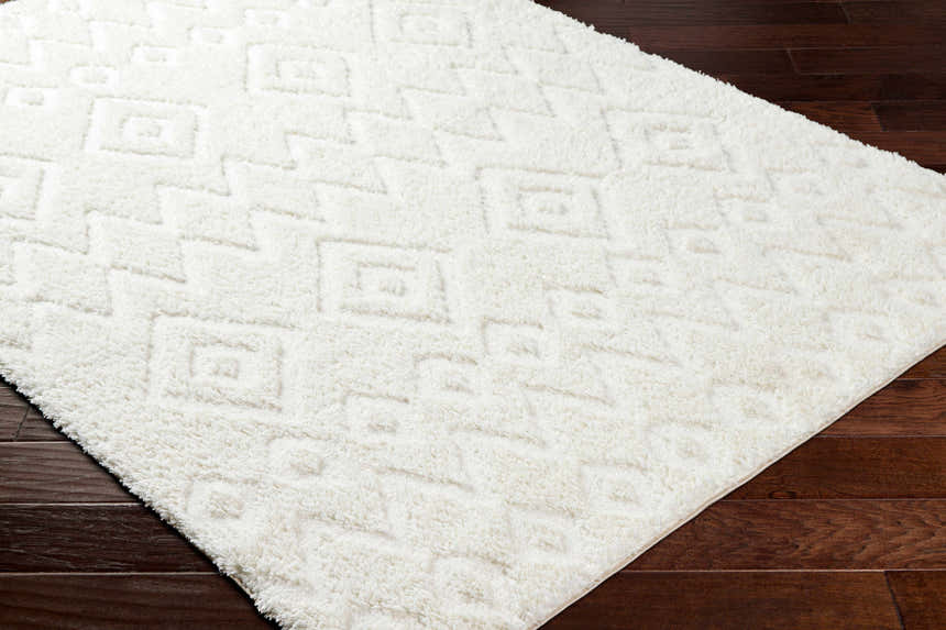 Close-up of the plush, white Hoshi Area Rug with a geometric shag design on dark wood flooring. Corner
