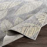 Close-up of the Snook Area Rug showing its beige and gray leaf pattern and machine-woven texture. Fold