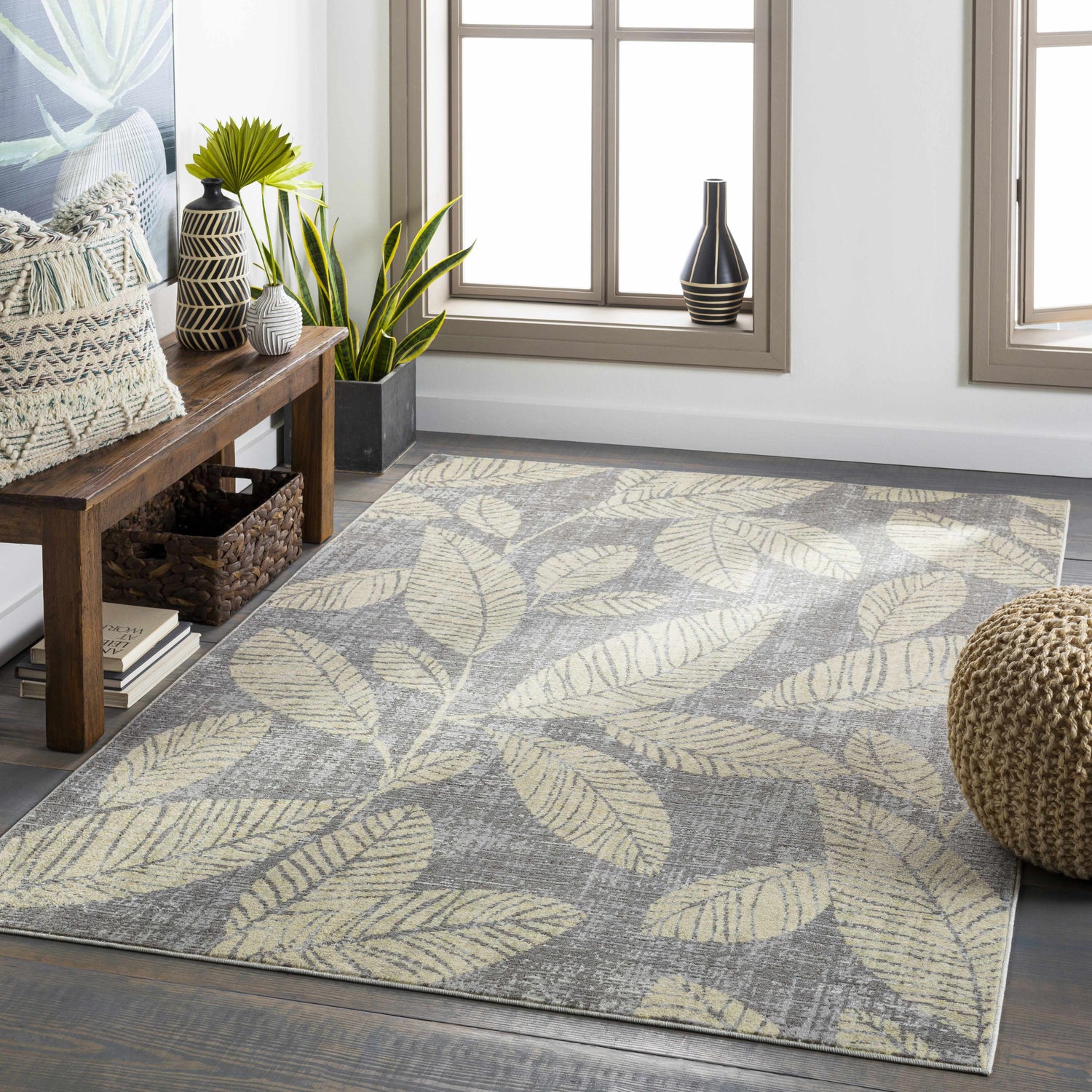 Living room scene with a gray Snook Area Rug featuring a beige leaf pattern, wood bench, and natural light. Roomscene-Rectangle