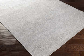 Close-up of the light slate Snover Carpet Area Rug showing its hand-woven texture and color on dark wood flooring. Corner