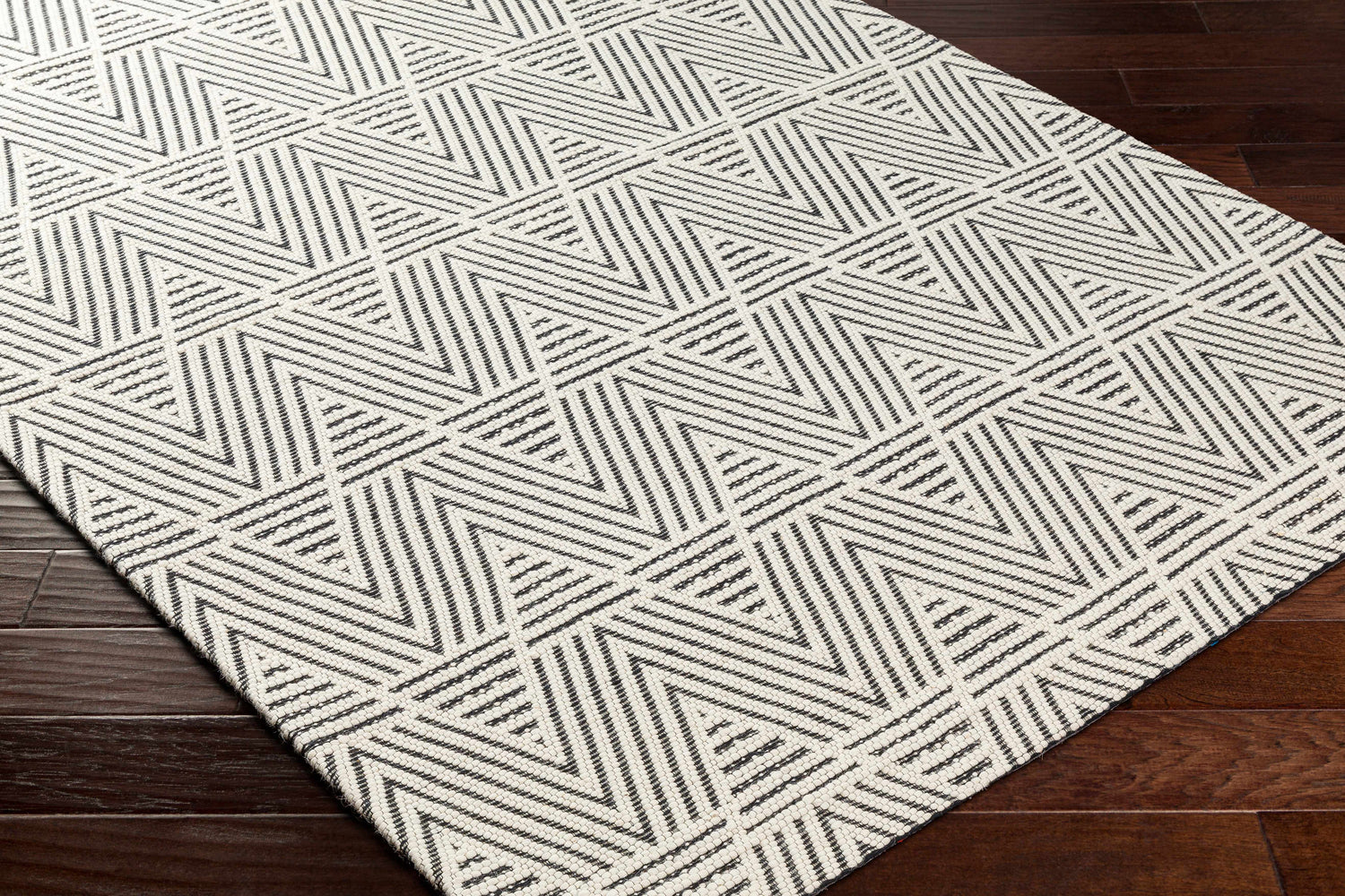 Close-up of Dawid Wool Area Rug with geometric black and bone triangle pattern on dark wood floor. Corner