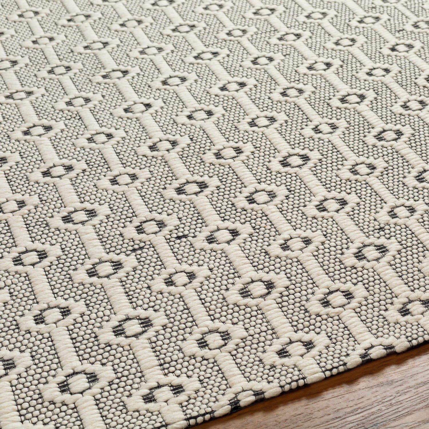 Close-up of the Puna Area Rug, showing a hand-woven black and bone geometric pattern and textured wool detail. Texture