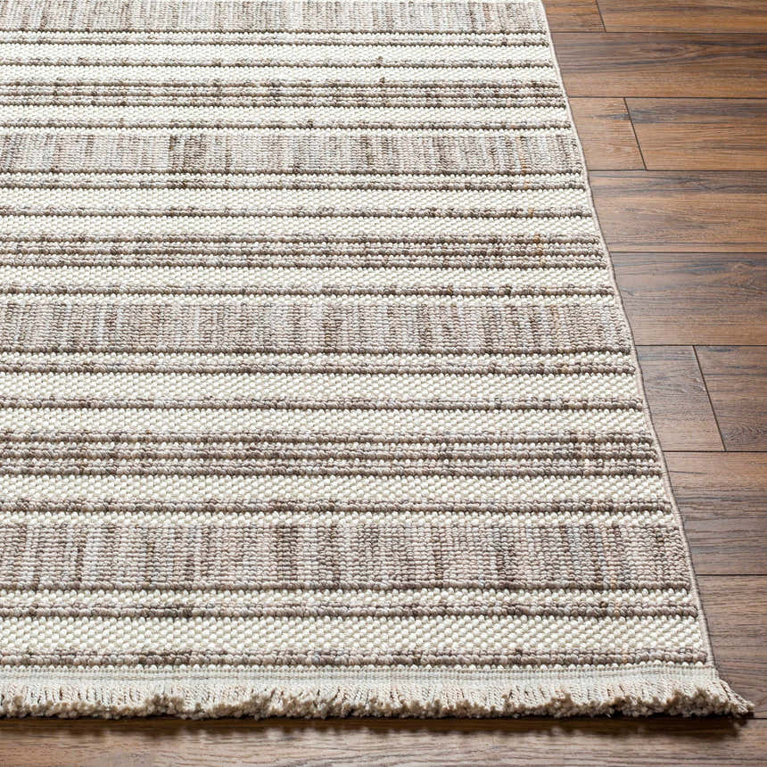 Close-up of Avari Area Rug showing beige and brown stripes, woven texture, and fringe detail on a wood floor. Front