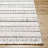 Close-up of Dagan Area Rug. Beige and driftwood tones with geometric pattern and fringe detail on a wood floor. Front