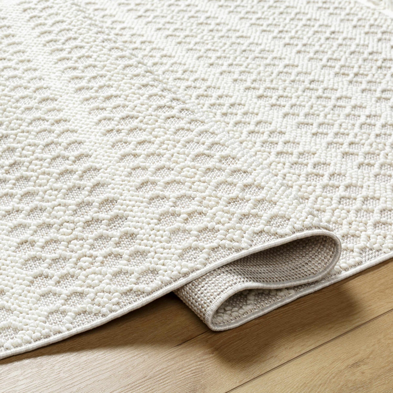 Close-up of the Hamal Area Rug, showing a textured, geometric pattern in cloud gray and cream on a light wood floor. Fold