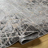 Close-up of the Luol Gray Area Rug showing its charcoal, gray, and natural geometric pattern and soft polyester texture. Fold