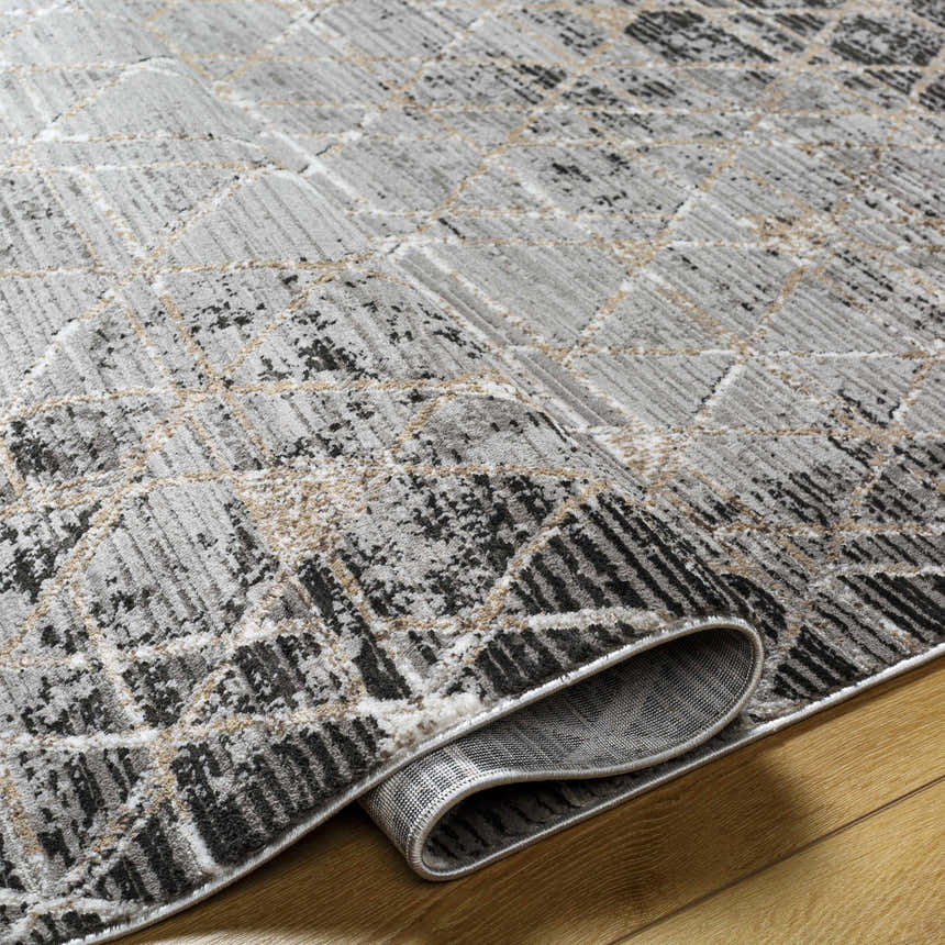 Close-up of the Luol Gray Area Rug showing its charcoal, gray, and natural geometric pattern and soft polyester texture. Fold