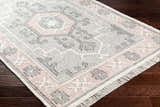 Close-up of the hand-woven Sosa Area Rug. Charcoal, cream, dusty pink, and light gray traditional design with fringe. Corner