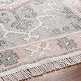 Close-up of the hand-woven Sosa Area Rug. Charcoal, cream, and dusty pink traditional pattern with fringe detail. Texture