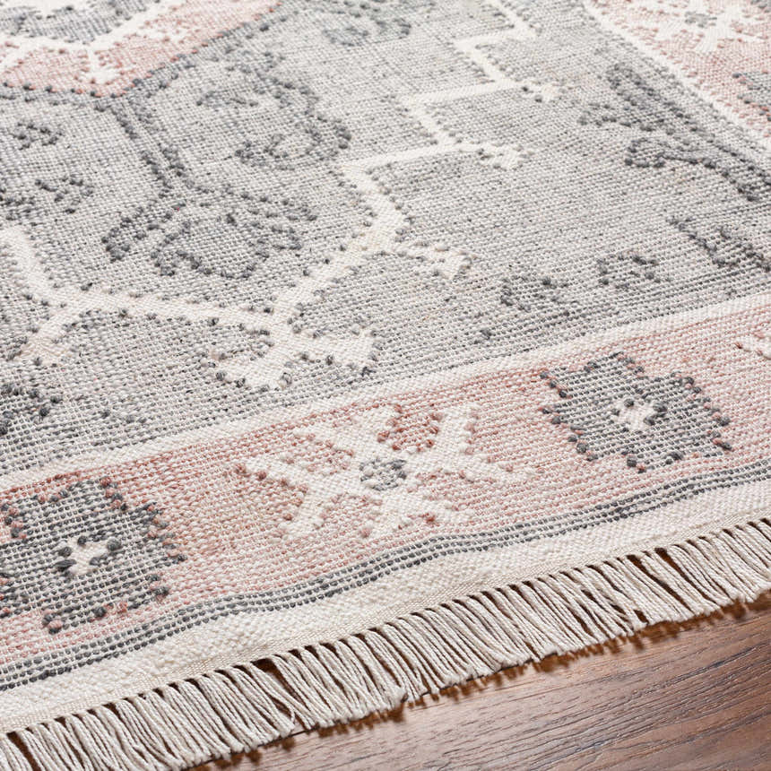 Close-up of the hand-woven Sosa Area Rug. Charcoal, cream, and dusty pink traditional pattern with fringe detail. Texture