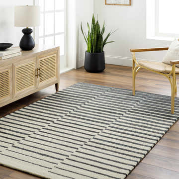 Living room scene with a Gawel Charcoal Area Rug, wood cabinet, gold chair, and potted plant. Roomscene-Rectangle