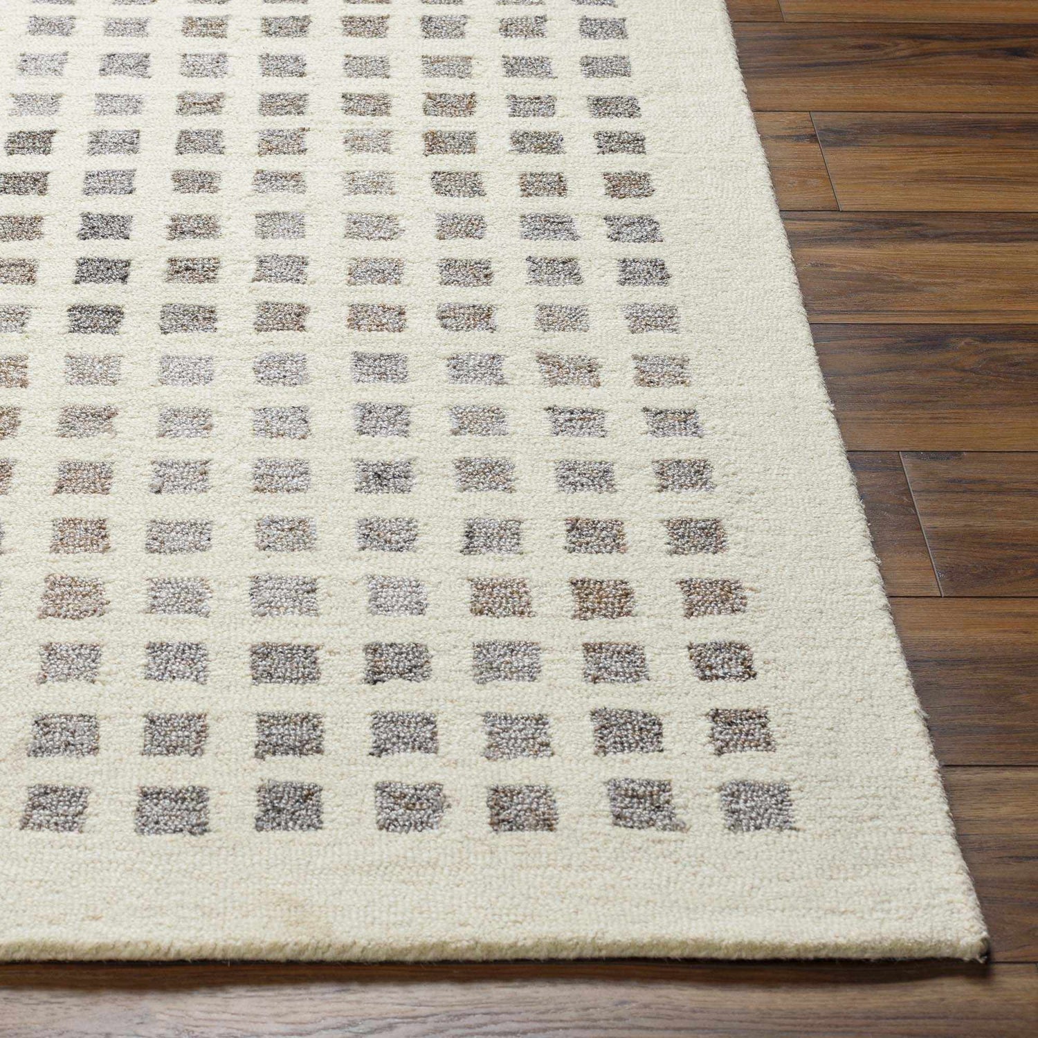 Close-up of the hand-tufted Harib Area Rug. Beige wool rug with a geometric pattern of brown and gray squares. Front