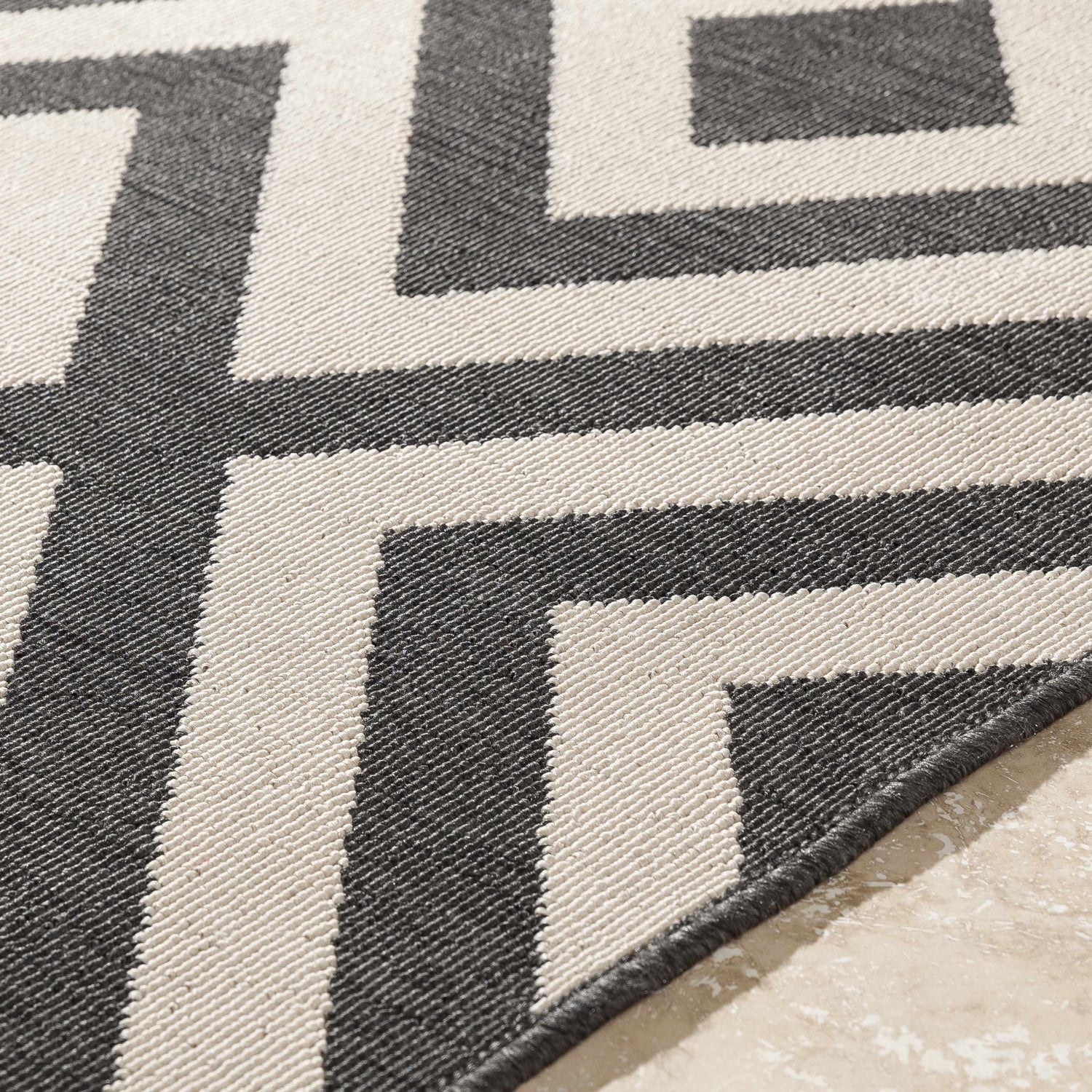 Close-up of the Spilsby Geometric Outdoor Rug. Black and light beige olefin rug with a modern geometric pattern. Texture