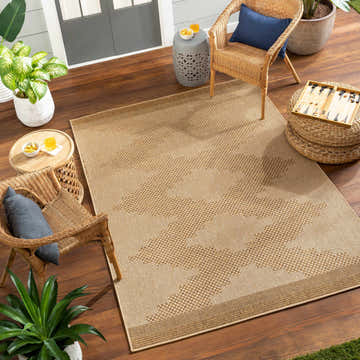 Outdoor patio scene with a Colum Flatweave Faux Jute Rug, wicker chairs, plants, and wood decking. The rug is beige and brown. Roomscene-Rectangle