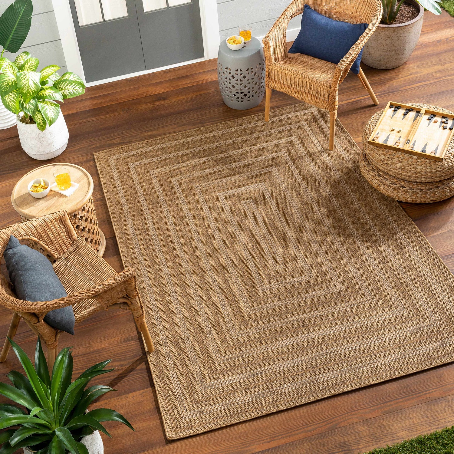 Outdoor patio scene with a camel Dyami Flatweave Faux Jute Rug, wicker chairs, and potted plants on a wood deck. Roomscene-Rectangle