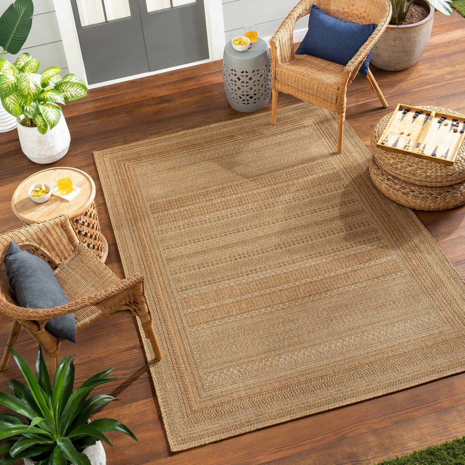 Outdoor patio scene with the beige Freja Flatweave Faux Jute Rug, wicker chairs, plants, and wood deck. Roomscene-Rectangle