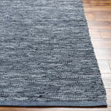 Close-up of the hand woven Aneko Gray Area Rug on wood floors. Features dark gray, light gray, and silver tones. Front