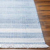 Close up of the hand woven Loic Silver Blue Area Rug showing its light blue stripes and fringe detail on a wood floor. Front