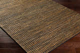 Close-up of the hand-woven Riki Black Area Rug showing jute texture and striped design on dark wood floor. Corner
