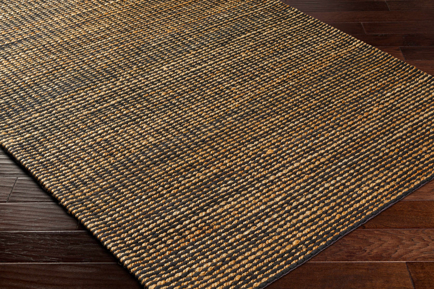 Close-up of the hand-woven Riki Black Area Rug showing jute texture and striped design on dark wood floor. Corner