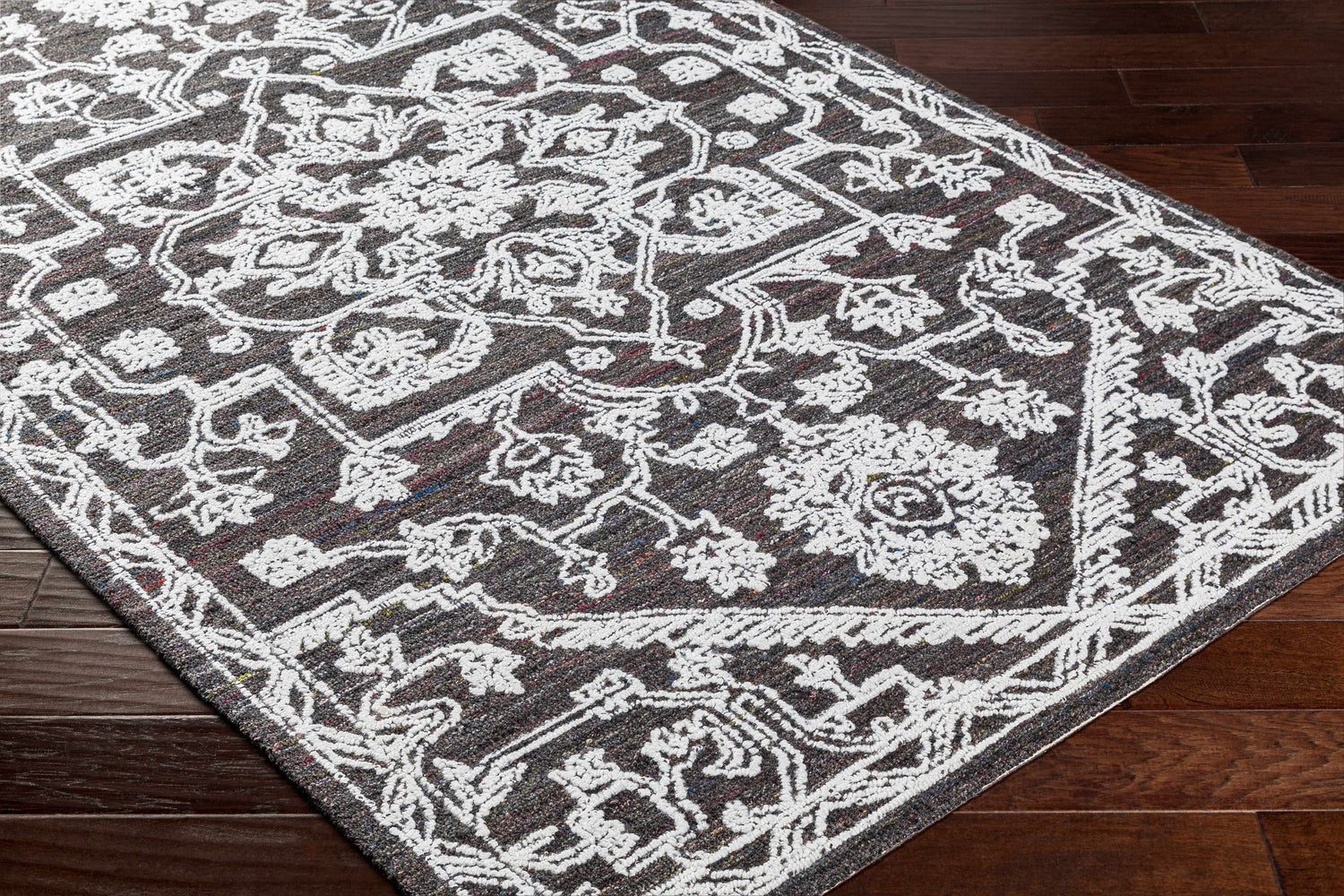 Close-up of the Black Derya Area Rug featuring a traditional floral pattern in light gray on a charcoal background. Corner