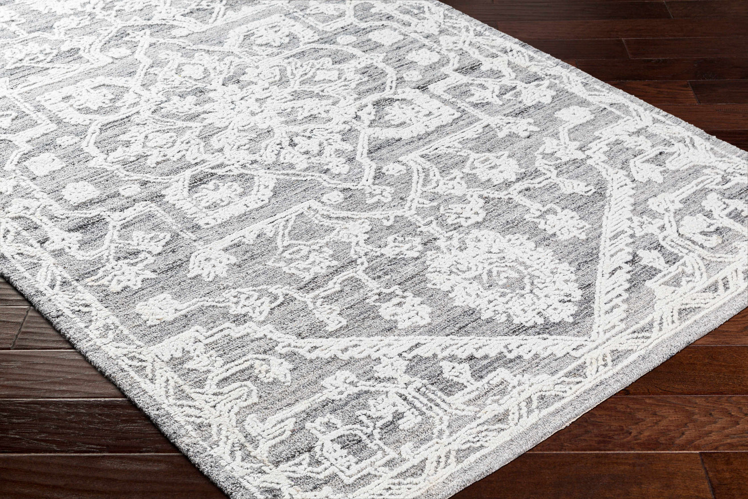 Close-up of the Blue Derya Area Rug showing its gray and white traditional pattern and hand-tufted texture on dark wood floors. Corner