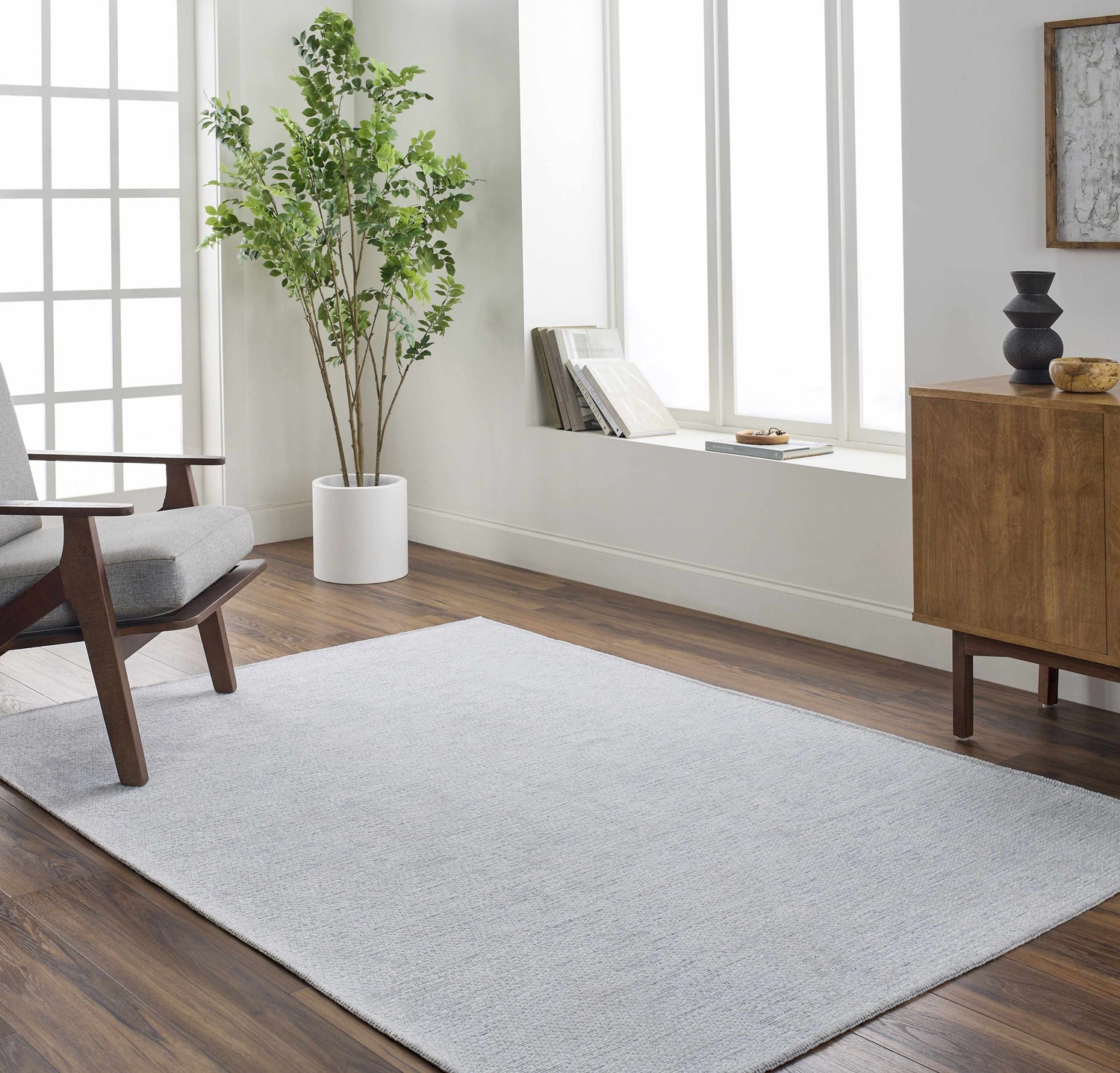 Living room scene with a light blue Isako Washable Rug, gray chair, wood cabinet, and indoor tree. Roomscene-Rectangle