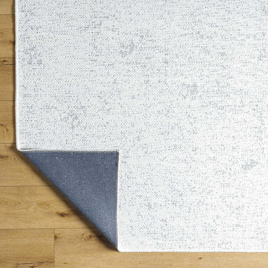 Close-up of Isako Cream & Gray Solid Washable Area Rug showing texture, colors, and blue backing on wood floor. Fold