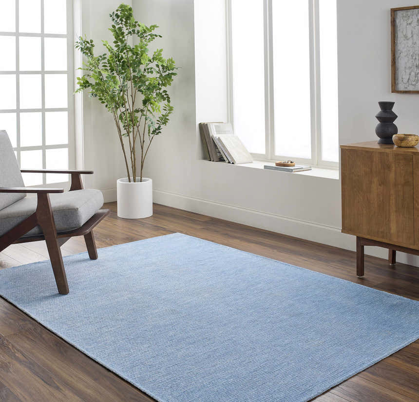 Living room scene with light blue Isako Washable Area Rug, gray chair, wood cabinet, and large window. Roomscene-Rectangle