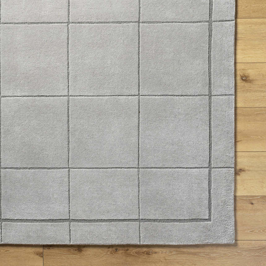 Close-up of the light gray, hand-tufted Siarl Gray Checkered Area Rug on a wood floor. 100% wool texture detail. Corner