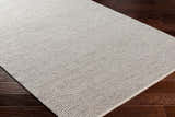 Close-up of the Blaga Area Rug in cloud gray, showing its hand-woven texture and contemporary design on dark wood floors. Corner