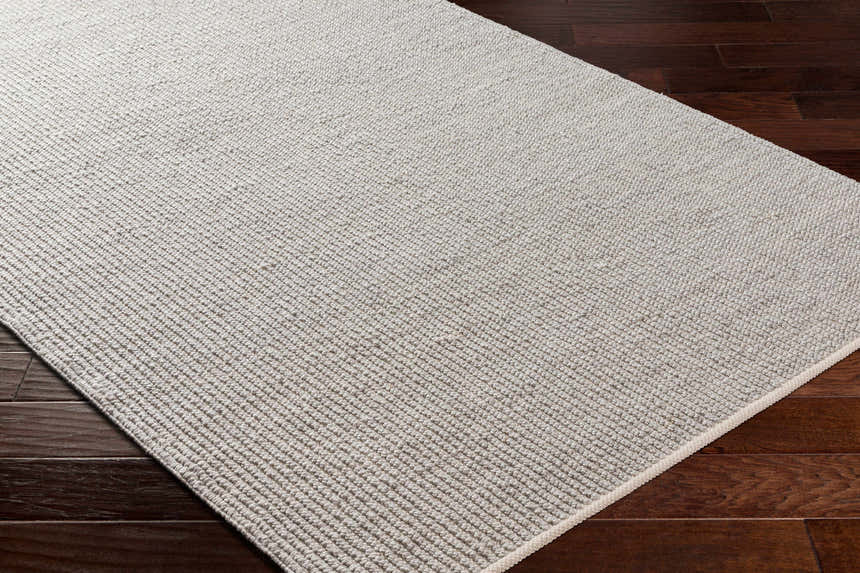 Close-up of the Blaga Area Rug in cloud gray, showing its hand-woven texture and contemporary design on dark wood floors. Corner