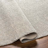 Close-up of the hand woven Blaga Area Rug showing its cloud gray color and textured, looped design. Fold