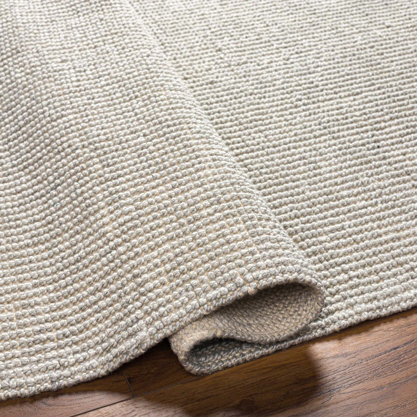 Close-up of the hand woven Blaga Area Rug showing its cloud gray color and textured, looped design. Fold