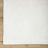 Close-up of the hand-tufted Nazih Area Rug in light silver and off-white on a light wood floor. Contemporary style. Corner