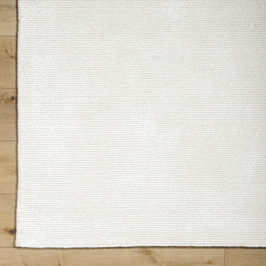 Close-up of the hand-tufted Nazih Area Rug in light silver and off-white on a light wood floor. Contemporary style. Corner