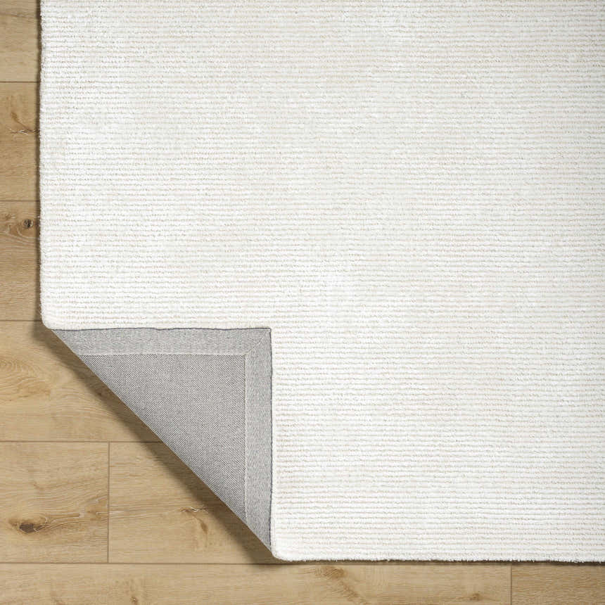 Close-up of the light silver Nazih Area Rug showing texture and backing on a wood floor. Fold