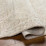 Close-up of the beige Huong Area Rug showing its textured, contemporary design and rolled edge on hardwood floor. Fold