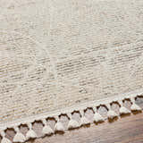Close-up of the beige Huong Area Rug showing its subtle geometric pattern and decorative tassel fringe. Texture