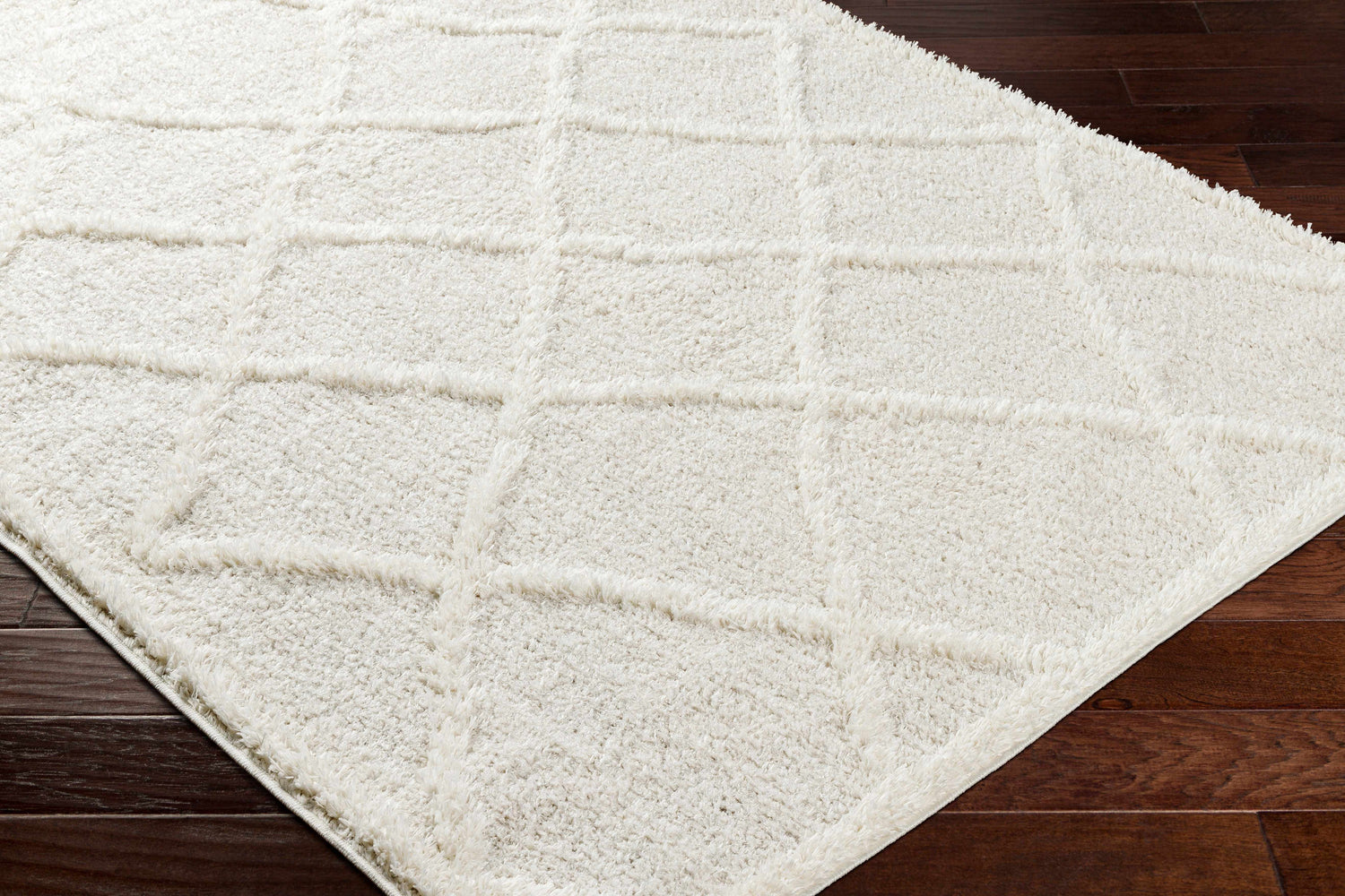 Close-up of the plush Daube Area Rug in cloud gray with a subtle geometric pattern on dark wood flooring. Corner