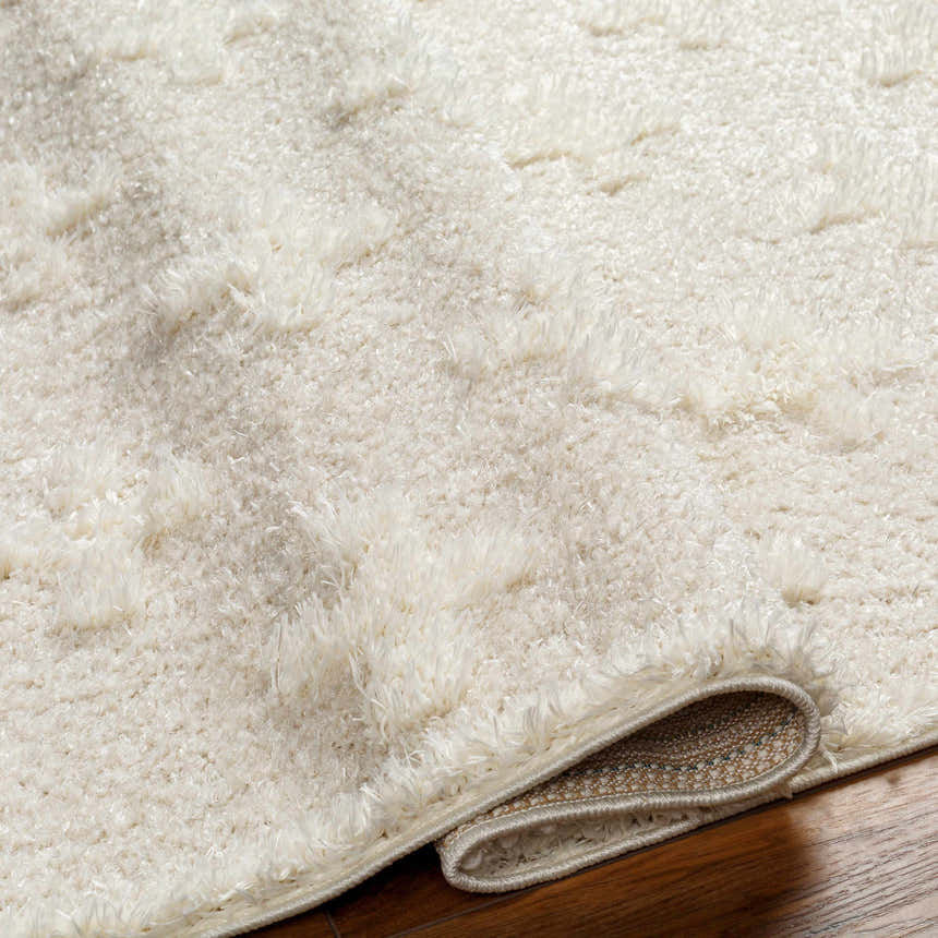 Close-up of the cream Satu Area Rug showing its shag texture and geometric pattern on a dark wood floor. Fold
