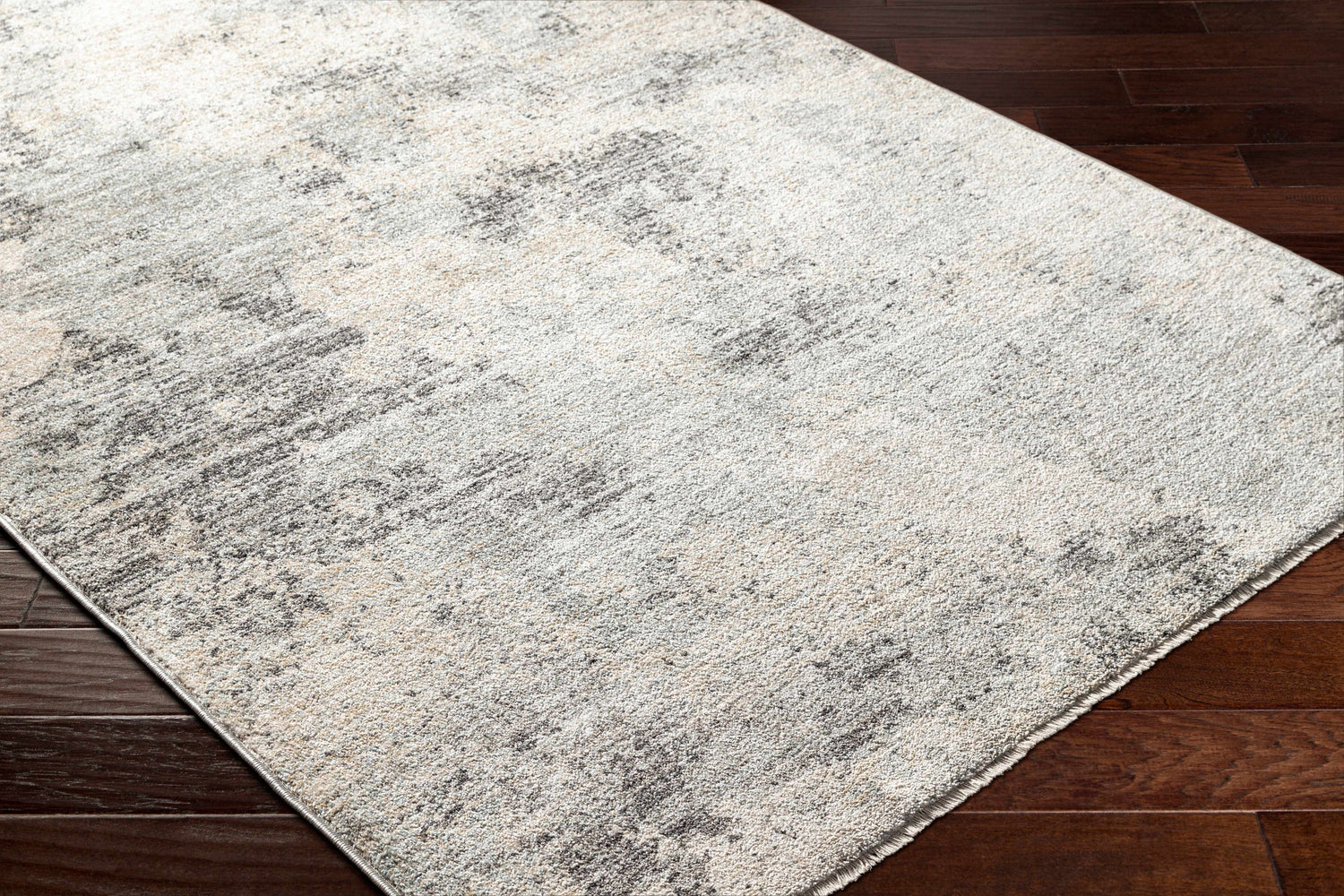 Close-up of the Gatik Area Rug, a contemporary design in beige, gray, and brown tones on dark wood flooring. Corner