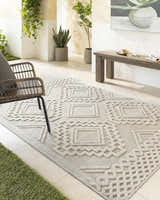 Stylish patio scene with a bone-colored Arwid Bone Area Rug, wicker chair, and wood bench. Neutral tones and geometric pattern. Roomscene-Rectangle